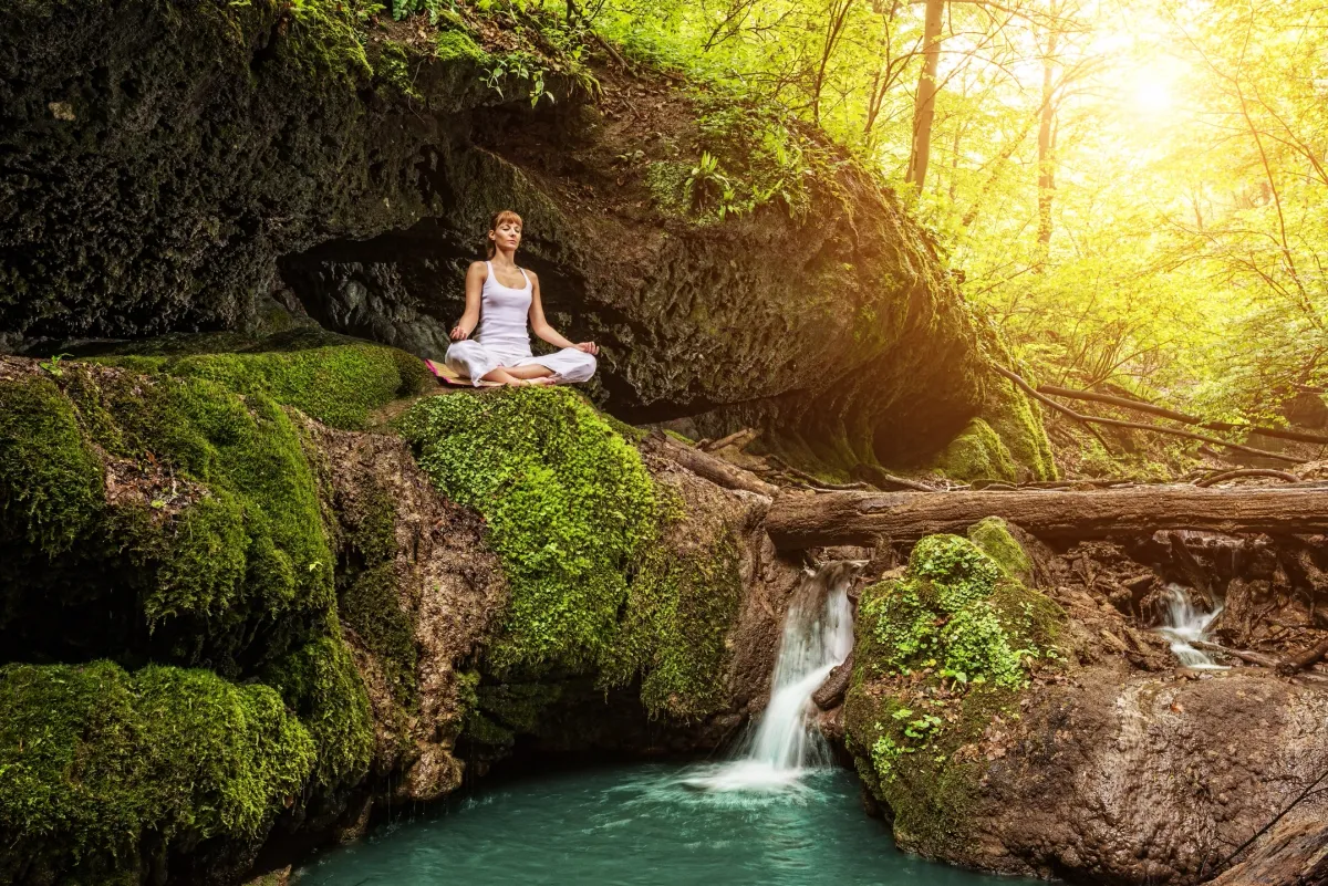 Woman meditating quietly by a mossy waterfall grotto