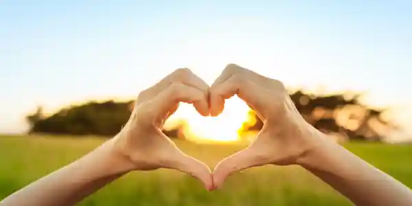 Two hands forming a heart at sunset, a quiet symbol of the connection at the heart of Yanssima